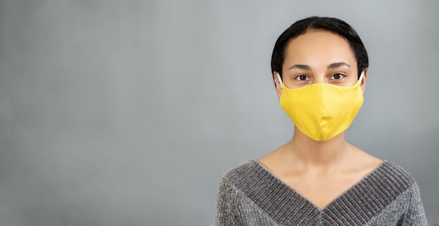 Close up of a young woman with a yellow mask on her face against SARS-cov-2. Gray wall. Copy space.  Color trends of 2021. Positive concept