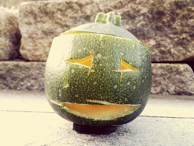 Photo close-up of zucchini jack o lantern on floor against wall