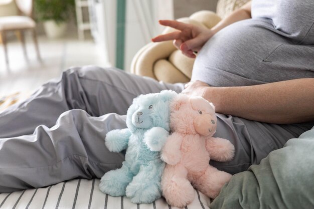Close-up zwangere vrouwelijke buik met berenspeelgoed gebaren twee vingers in afwachting van een tweeling babyjongen en meisje