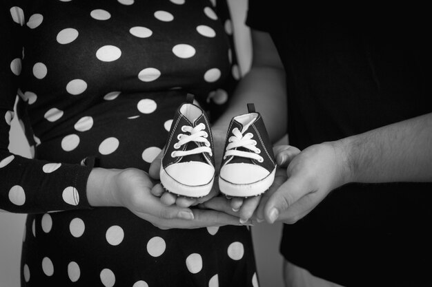 Close-up zwart-wit foto van aanstaande ouders met baby laarzen op handen