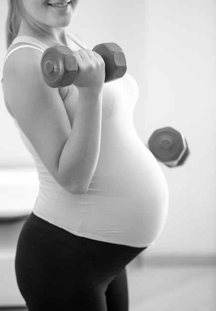 Close-up zwart-wit foto van zwangere vrouw die dumbbells optilt