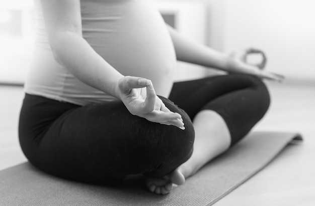 Close-up zwart-wit foto van zwangere vrouw die thuis yoga beoefent op de vloer