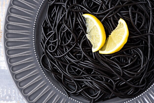 Close-up zwarte spaghetti met inktinktvissen met citroen op grijze plaat op grijze achtergrond met exemplaarruimte, zwart deegwarenconcept