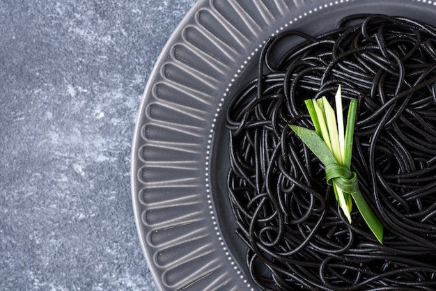 Close-up zwarte spaghetti met inktinktvissen met groen blad op grijze plaat op grijze achtergrond met exemplaarruimte, zwart deegwarenconcept