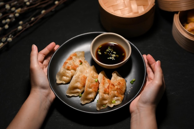 Close-upbeeld een vrouwelijke handen die een bord smakelijke gefrituurde dumplings over moderne zwarte tafel houden