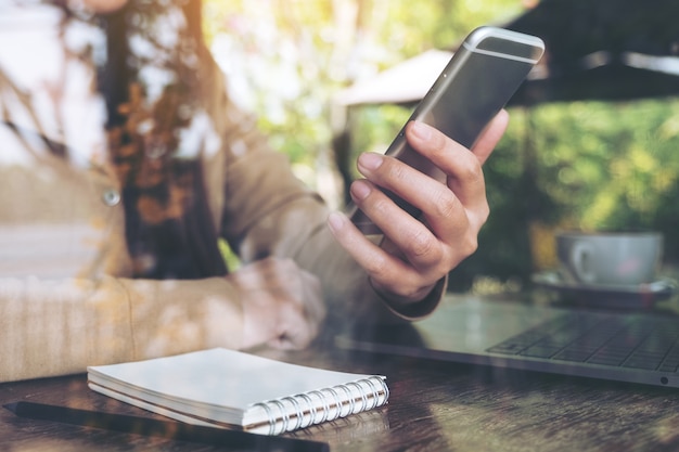 Close-upbeeld van de hand die van de vrouw en slimme telefoon houden bekijken terwijl het gebruiken van laptop