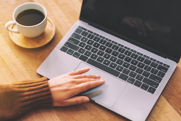 Close-upbeeld van de hand van een vrouw die laptop-touchpad op houten tafel gebruikt en aanraakt