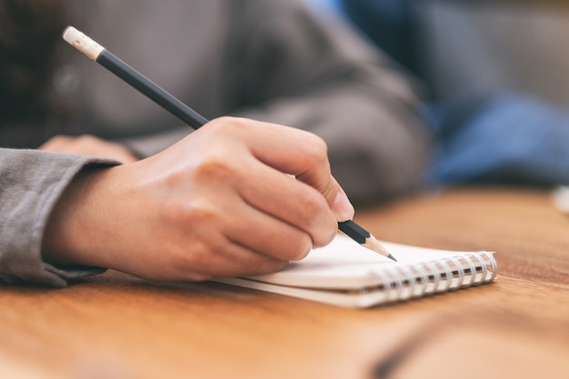 Close-upbeeld van de hand van een vrouw die op blanco notitieboekje op houten tafel schrijft