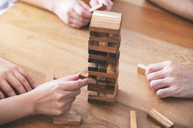 Foto close-upbeeld van drie vrienden die samen tumble tower houten blokspel zitten en spelen