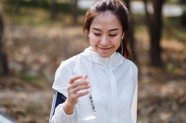 Close-upbeeld van een Aziatische sportvrouw die een waterfles vasthoudt na het joggen in het stadspark