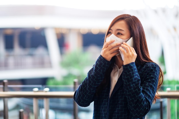 Close-upbeeld van een Aziatische vrouw die beschermend gezichtsmasker draagt, die op mobiele telefoon voor gezondheidszorg en Covid-19-concept gebruikt en praat