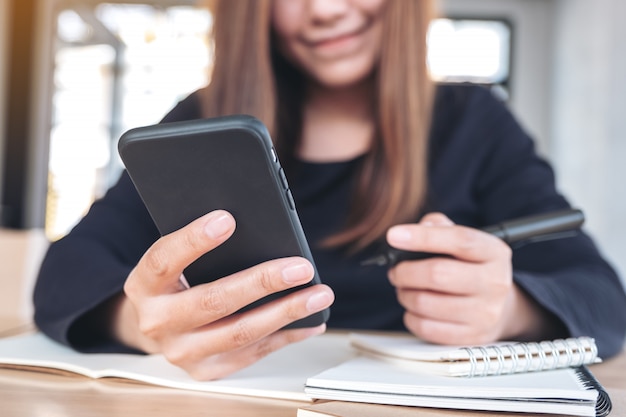 Close-upbeeld van een Aziatische vrouw die slimme telefoon vasthoudt, gebruikt en bekijkt tijdens het werken en schrijven