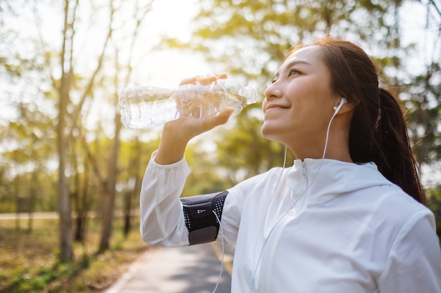 Close-upbeeld van een Aziatische vrouwelijke hardloper die water uit fles drinkt na het joggen in het stadspark