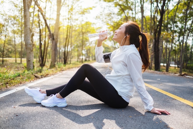 Close-upbeeld van een Aziatische vrouwelijke hardloper die water uit fles drinkt na het joggen in het stadspark