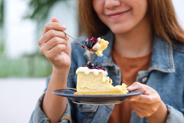 Close-upbeeld van een jonge Aziatische vrouw die bosbessenkaastaart eet