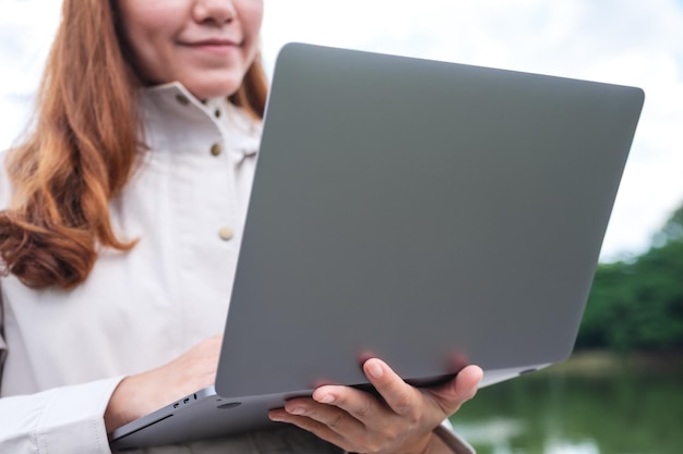 Close-upbeeld van een jonge Aziatische vrouw die laptopcomputer in de buitenlucht vasthoudt en gebruikt