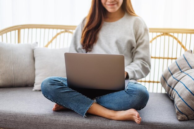 Close-upbeeld van een jonge vrouw die een laptopcomputer gebruikt en eraan werkt terwijl ze thuis op een bank zit