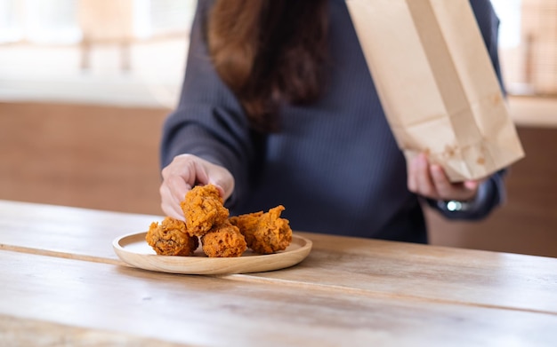 Close-upbeeld van een jonge vrouw die gebakken kip uit een papieren voedselzak plukt en thuis een bord inbrengt voor het concept van voedselbezorging