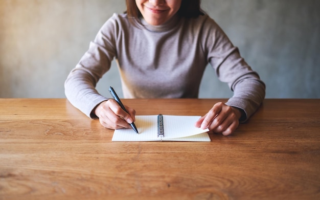 Close-upbeeld van een jonge vrouw die op een leeg notitieboekje op tafel schrijft