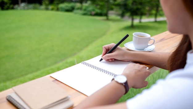 Close-upbeeld van een jonge vrouw die op een notitieboekje in de buitenlucht schrijft