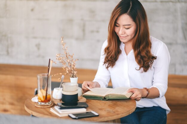 Close-upbeeld van een mooie aziatische vrouw die een boek vasthoudt en leest terwijl ze in café zit