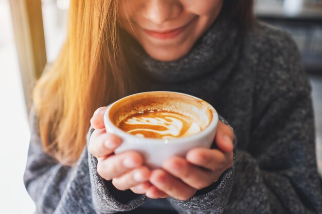 Close-upbeeld van een mooie Aziatische vrouw die een kop hete koffie houdt