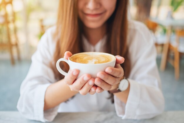 Close-upbeeld van een mooie Aziatische vrouw die een kop hete koffie houdt