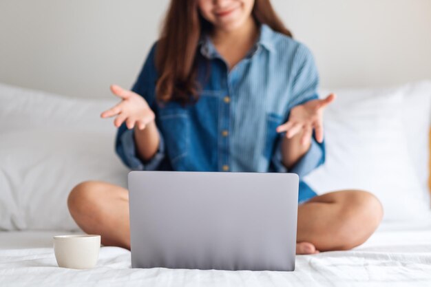 Close-upbeeld van een mooie Aziatische vrouw die een laptopcomputer gebruikt voor videogesprekken terwijl ze thuis op een bed zit