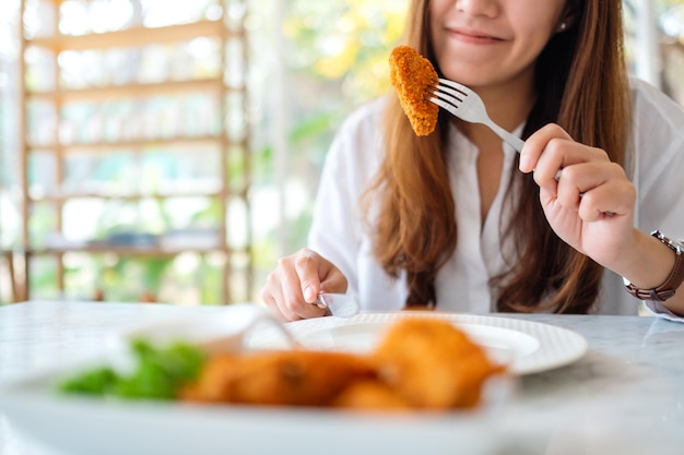 Close-upbeeld van een mooie Aziatische vrouw die gebraden kip door vork in restaurant eet