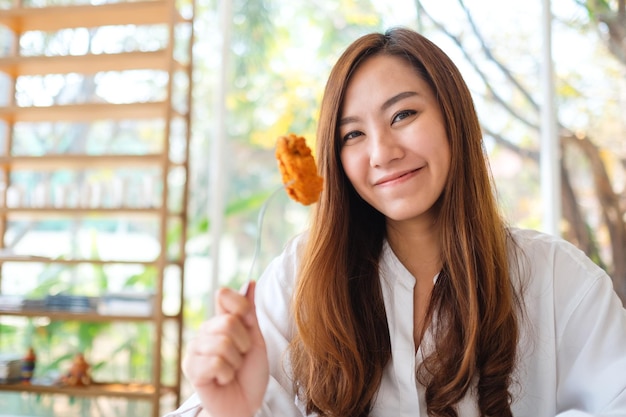 Close-upbeeld van een mooie aziatische vrouw die gebraden kip in restaurant toont en eet
