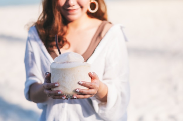 Close-upbeeld van een mooie aziatische vrouw die kokossap vasthoudt en drinkt op het strand