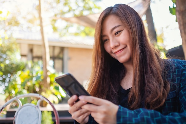 Close-upbeeld van een mooie Aziatische vrouw die mobiele telefoon in de buitenlucht vasthoudt, gebruikt en bekijkt