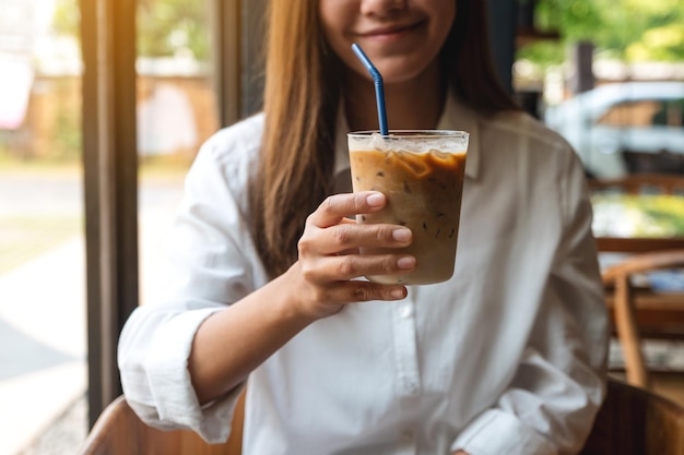 Close-upbeeld van een mooie jonge aziatische vrouw die een glas ijskoffie vasthoudt en toont