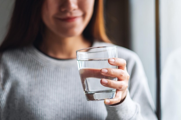 Close-upbeeld van een mooie jonge Aziatische vrouw die een glas water houdt om te drinken