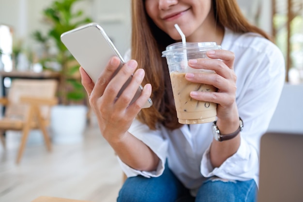 Close-upbeeld van een mooie jonge aziatische vrouw die een mobiele telefoon vasthoudt en gebruikt terwijl ze koffie drinkt in café