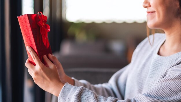 Foto close-upbeeld van een mooie jonge aziatische vrouw die een rode huidige doos vasthoudt en bekijkt