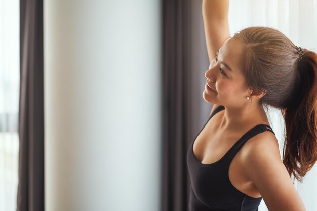 Close-upbeeld van een mooie jonge aziatische vrouw die haar armen uitrekt om op te warmen voordat ze thuis gaat trainen