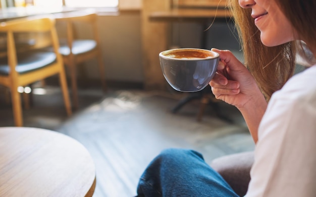 Close-upbeeld van een mooie jonge Aziatische vrouw die hete koffie houdt en drinkt