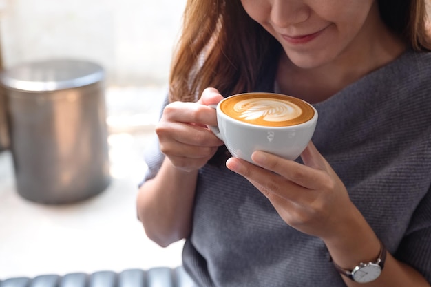 Close-upbeeld van een mooie jonge Aziatische vrouw die hete koffie ruikt en drinkt