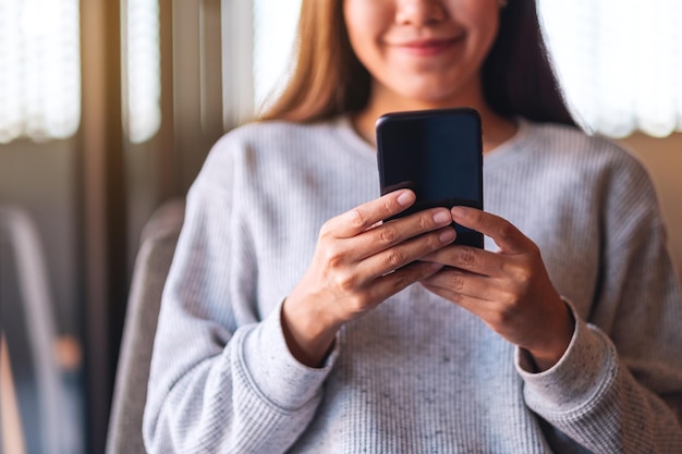 Close-upbeeld van een mooie jonge Aziatische vrouw die mobiele telefoon vasthoudt en gebruikt