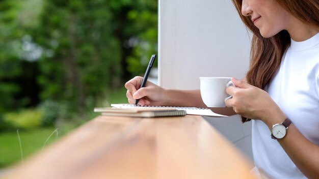 Close-upbeeld van een mooie jonge Aziatische vrouw die op een notitieboekje in de buitenlucht schrijft