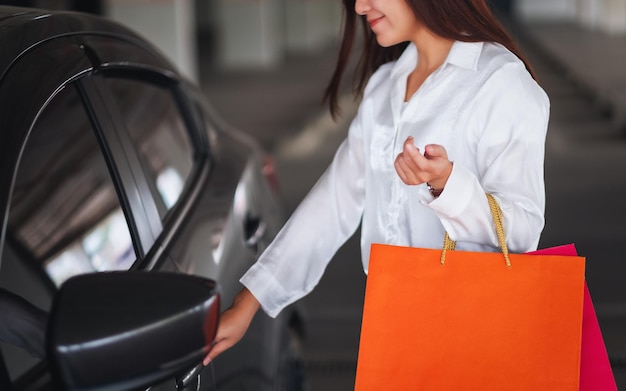 Close-upbeeld van een mooie vrouw die boodschappentassen vasthoudt terwijl ze de autodeur opent op de parkeerplaats van het winkelcentrum