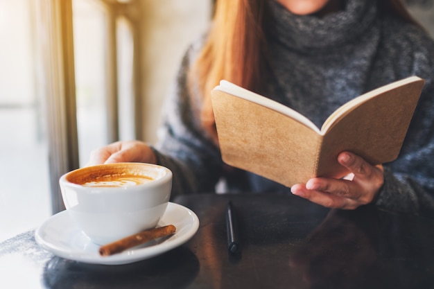 Close-upbeeld van een mooie vrouw die een boek leest terwijl ze 's ochtends koffie drinkt