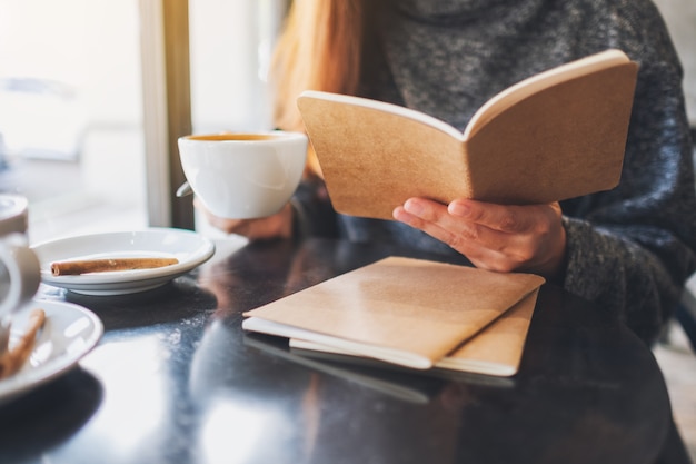 Close-upbeeld van een mooie vrouw die een boek leest terwijl ze 's ochtends koffie drinkt