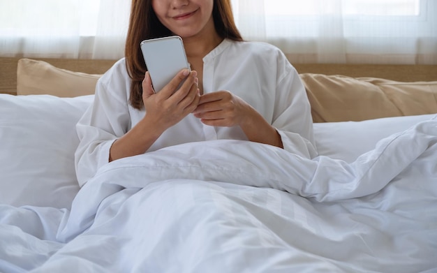 Close-upbeeld van een mooie vrouw die mobiele telefoon gebruikt terwijl ze op bed ligt