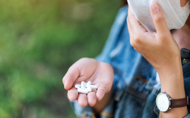 Foto close-upbeeld van een vrouw die een beschermend gezichtsmasker draagt en witte medicijncapsules in de hand houdt voor gezondheidszorg en covid-19 of 2020 virusconcept