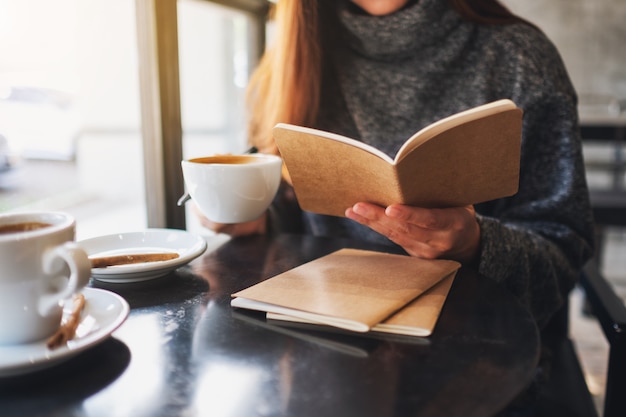 Close-upbeeld van een vrouw die een boek leest terwijl ze koffie drinkt in café