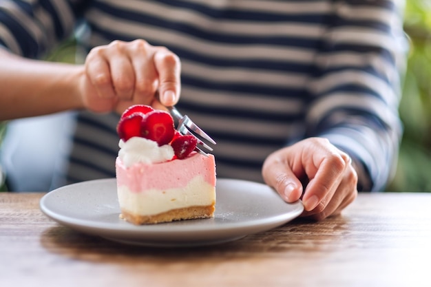 Close-upbeeld van een vrouw die een cake van de aardbeikaas in een bord eet