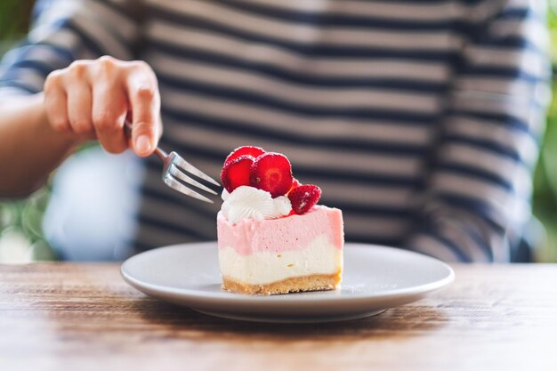 Close-upbeeld van een vrouw die een cake van de aardbeikaas in een bord eet