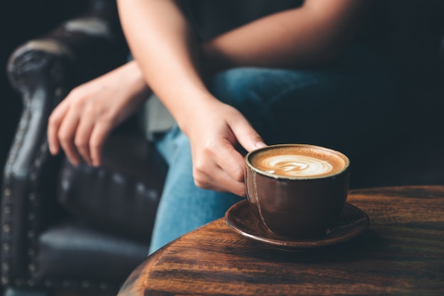 Close-upbeeld van een vrouw die een kopkoffie op uitstekende houten lijst in koffie houden